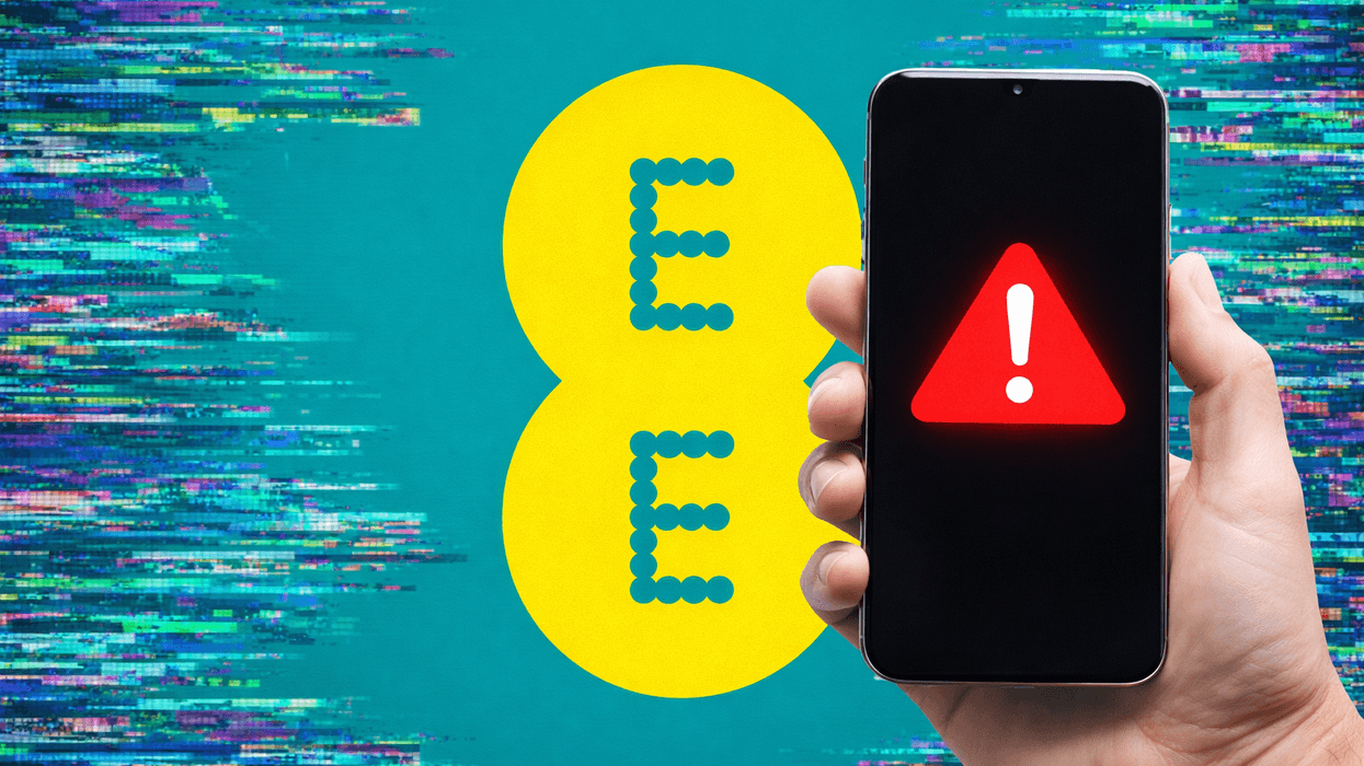 Hand holding mobile with warning symbol in front of EE logo