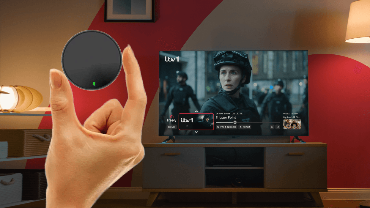 hand holding netgem pleio box with a television showing freely tv in the background