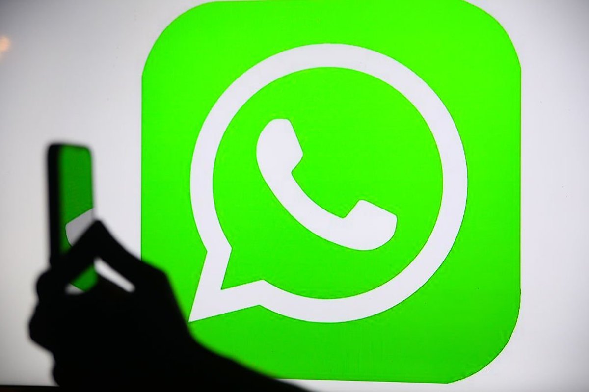 Hand holding phone in front of WhatsApp logo