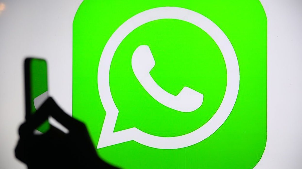 Hand holding phone in front of WhatsApp logo