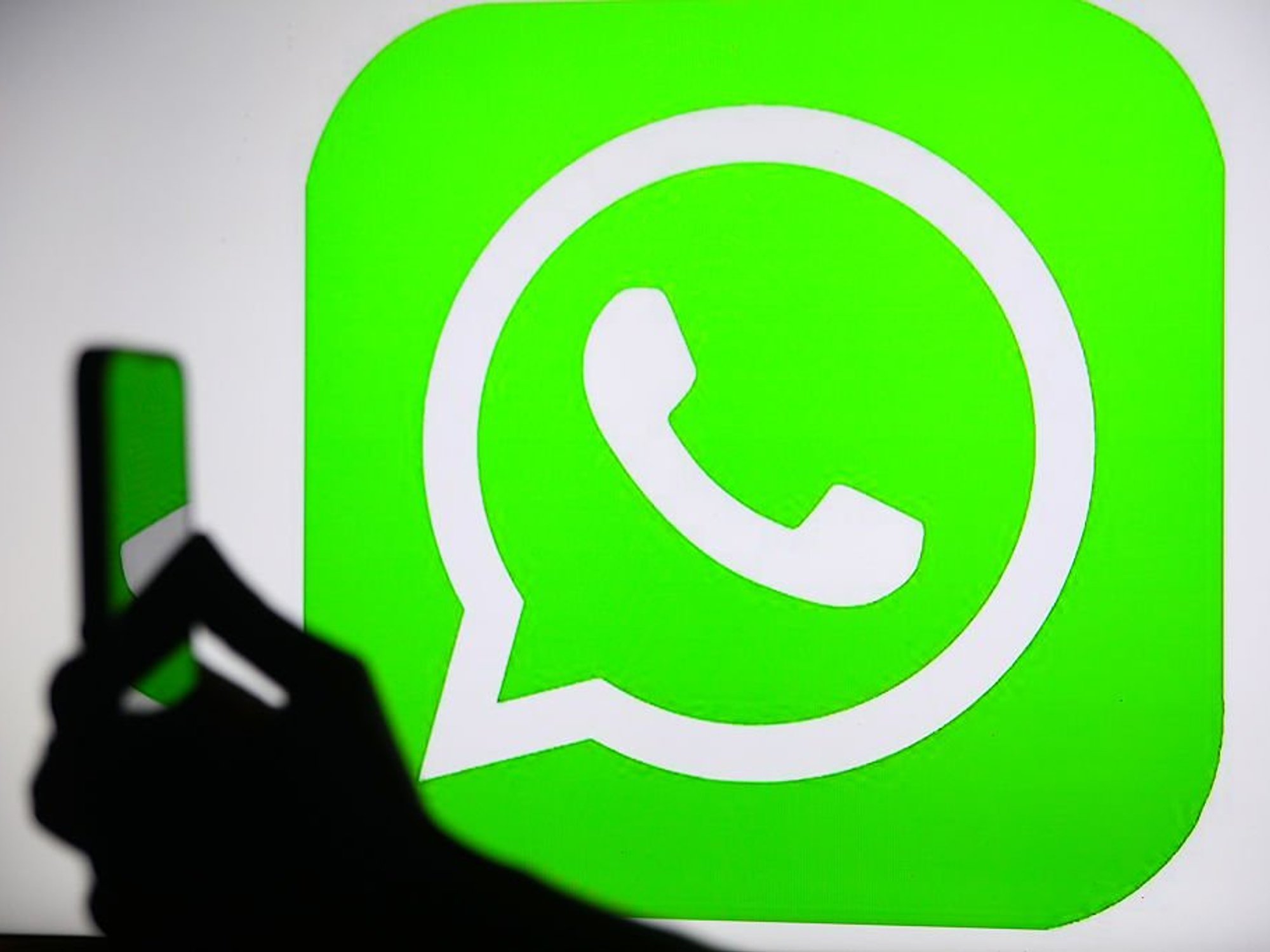 Hand holding phone in front of WhatsApp logo