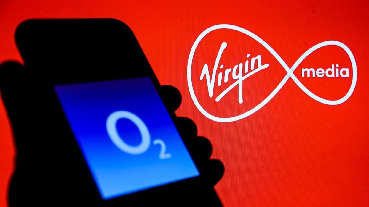 Hand holding phone with O2 logo displayed and Virgin Media logo displayed behind it