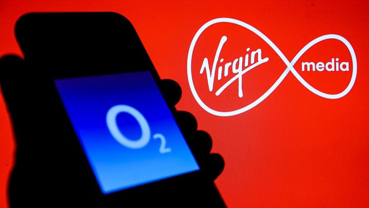 Hand holding phone with O2 logo displayed and Virgin Media logo displayed behind it