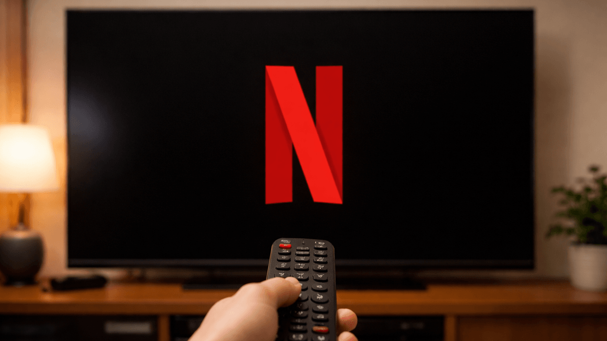 Hand holding remote in front of TV displaying Netflix logo