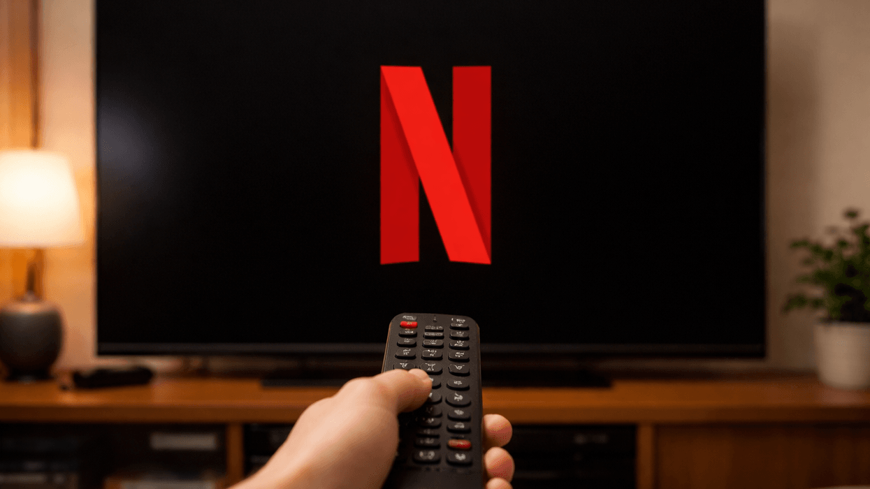 Hand holding remote in front of TV displaying Netflix logo