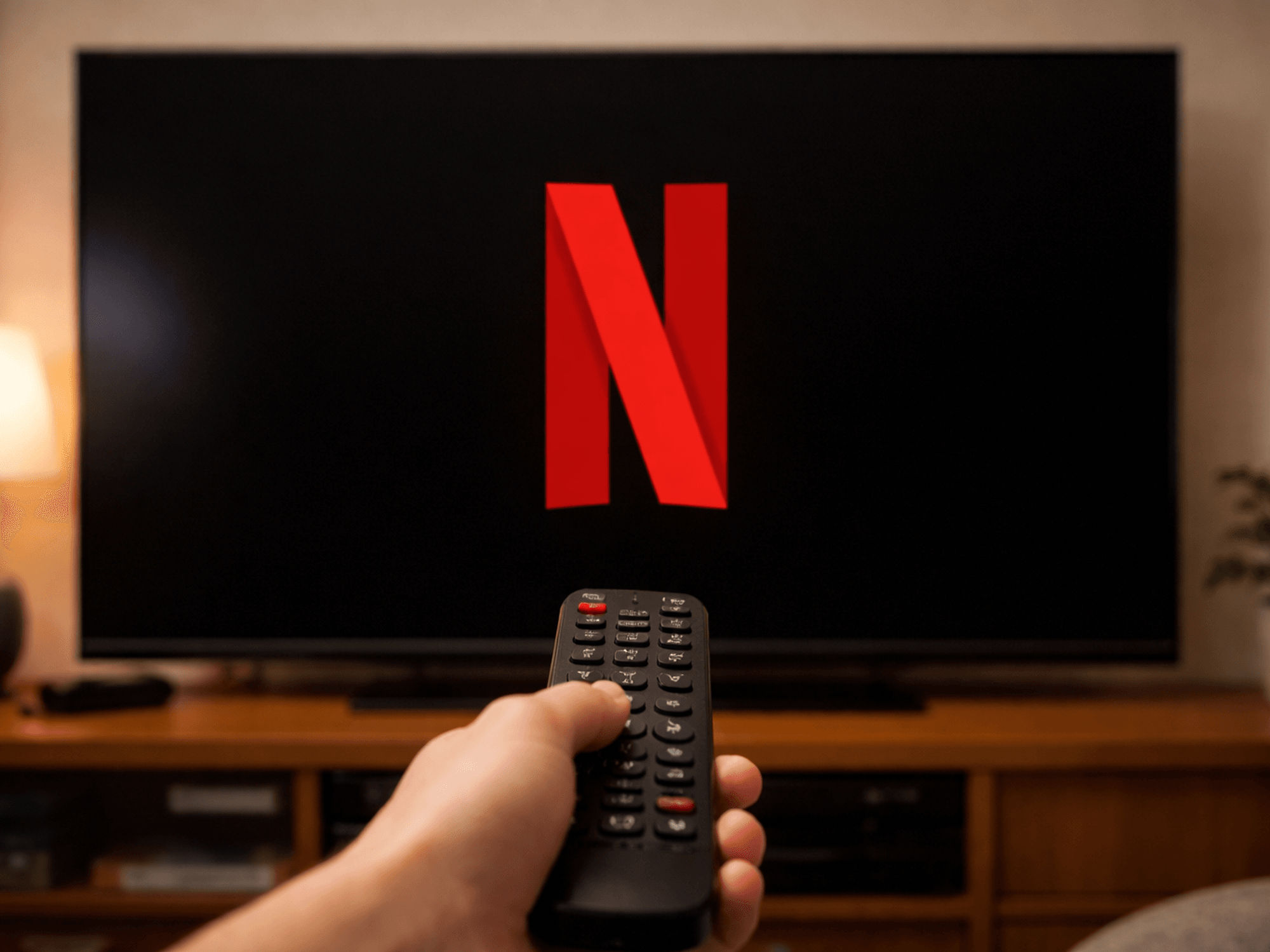 Hand holding remote in front of TV displaying Netflix logo