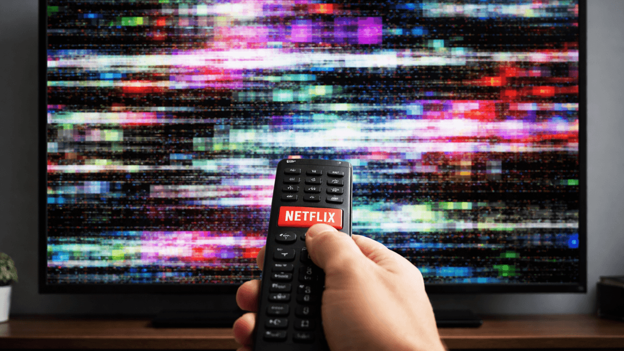 Hand holding remote with Netflix button pointed at non-working TV
