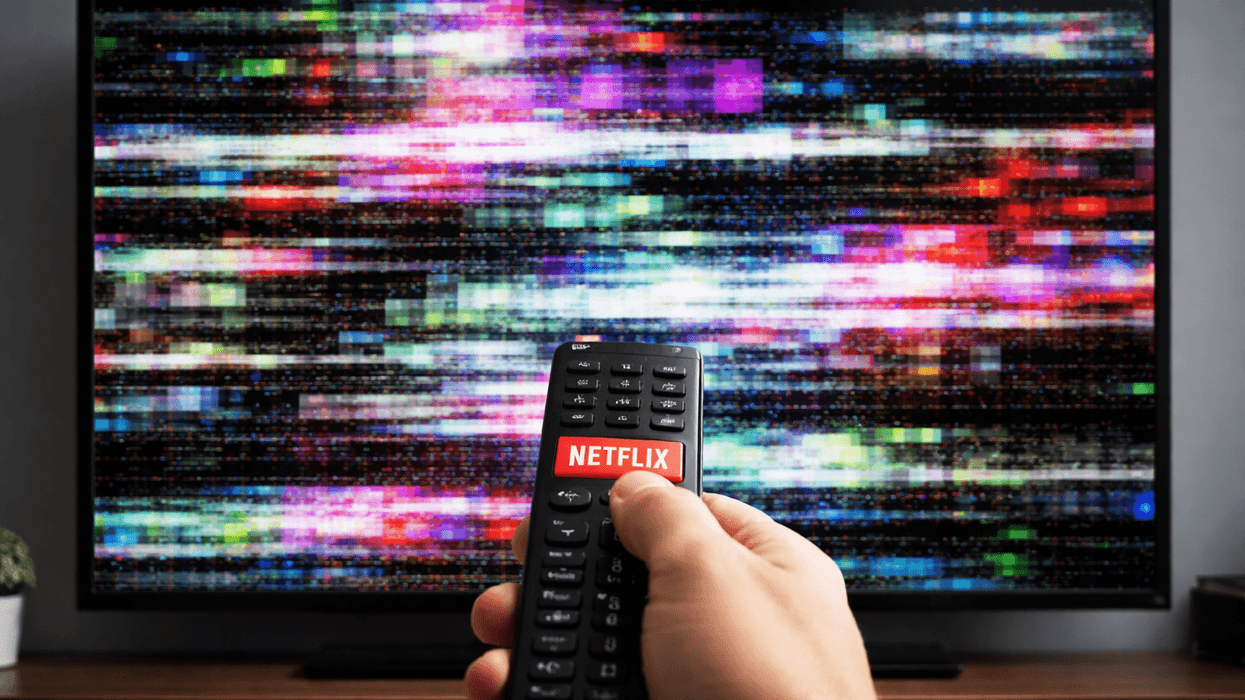 Hand holding remote with Netflix button pointed at non-working TV