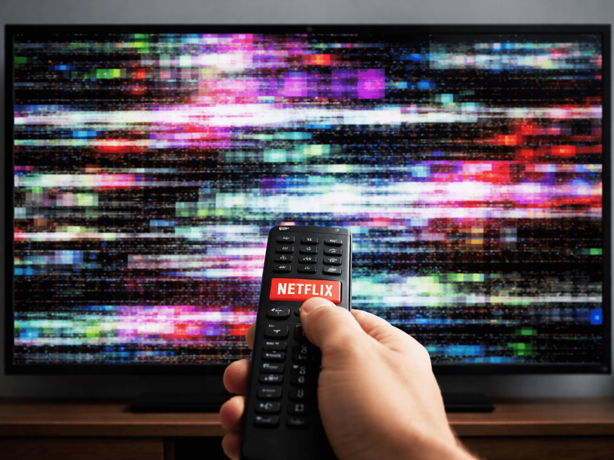 Hand holding remote with Netflix button pointed at non-working TV