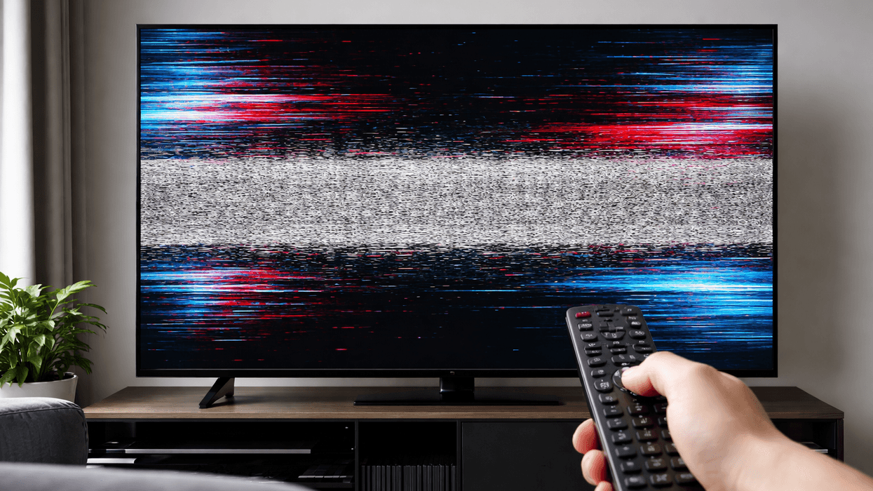 Hand holding TV remote in front of TV screen with a glitch