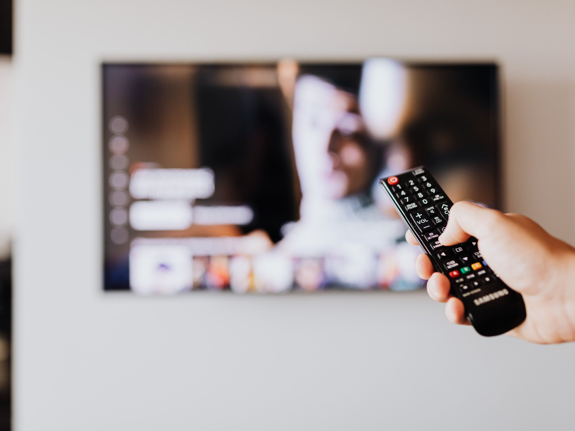 Hand holding TV remote in front of TV