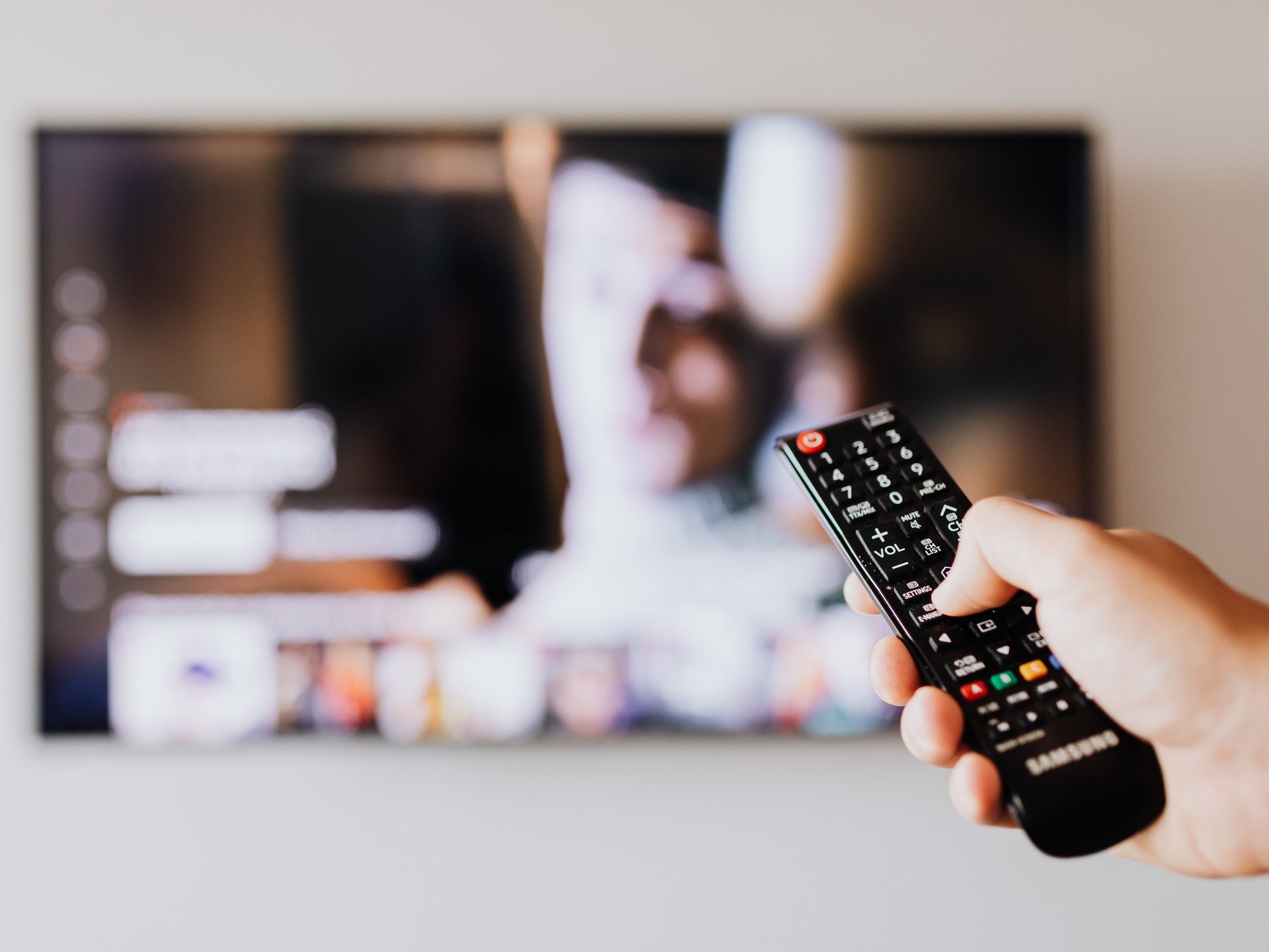 Hand holding TV remote in front of TV
