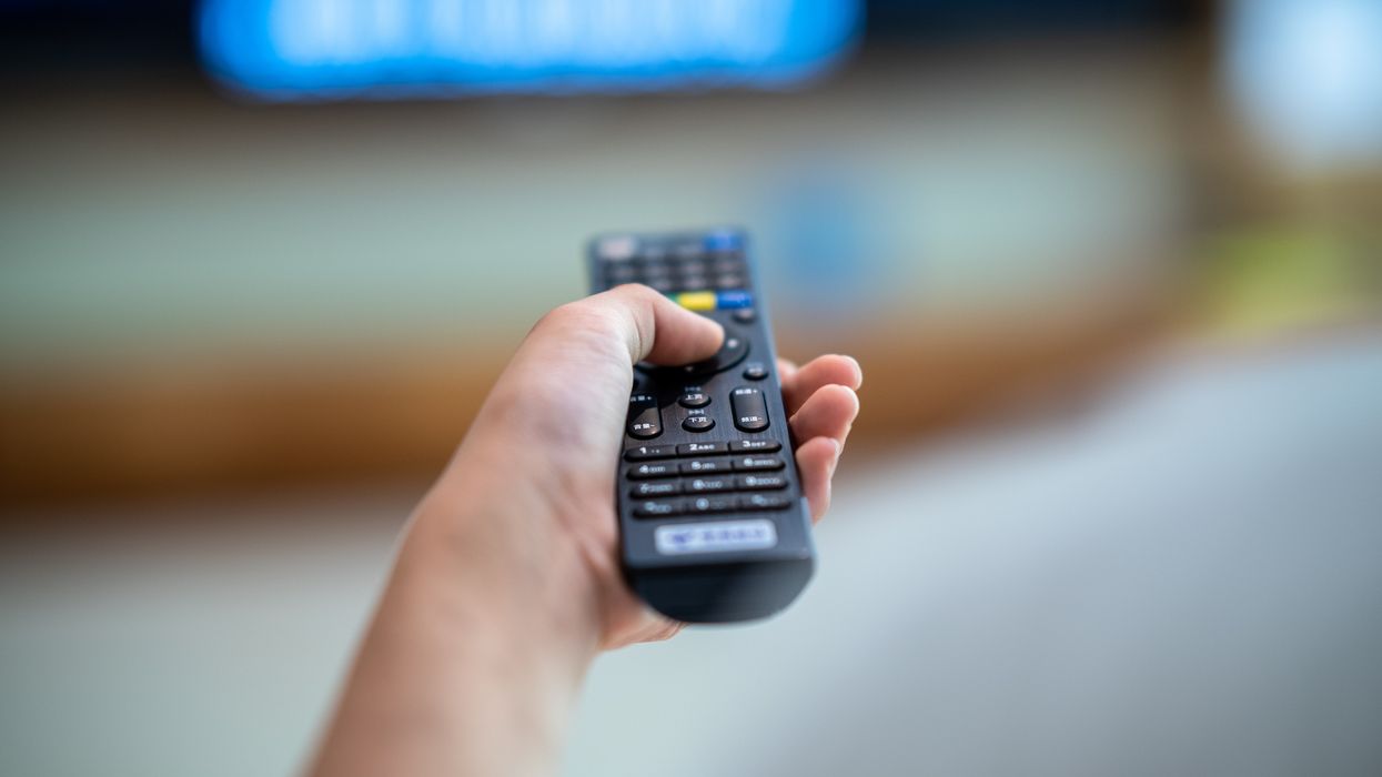 hand holds a remote control pointing at an out-of-focus smart tv in the background