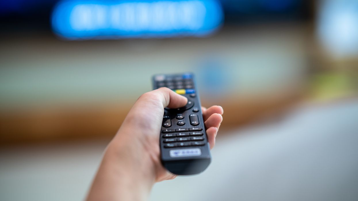 hand holds a remote control pointing at an out-of-focus smart tv in the background