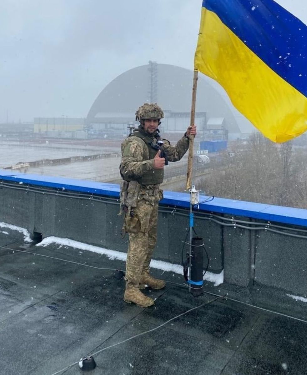 Handout photo issued by the Assault Troops of the Armed Forces of Ukraine of a Ukrainian soldier putting up the country's flag with a shelter containing the Chernobyl reactor that exploded in 1986 seen in the background. Picture date: Sunday April 3, 2022.