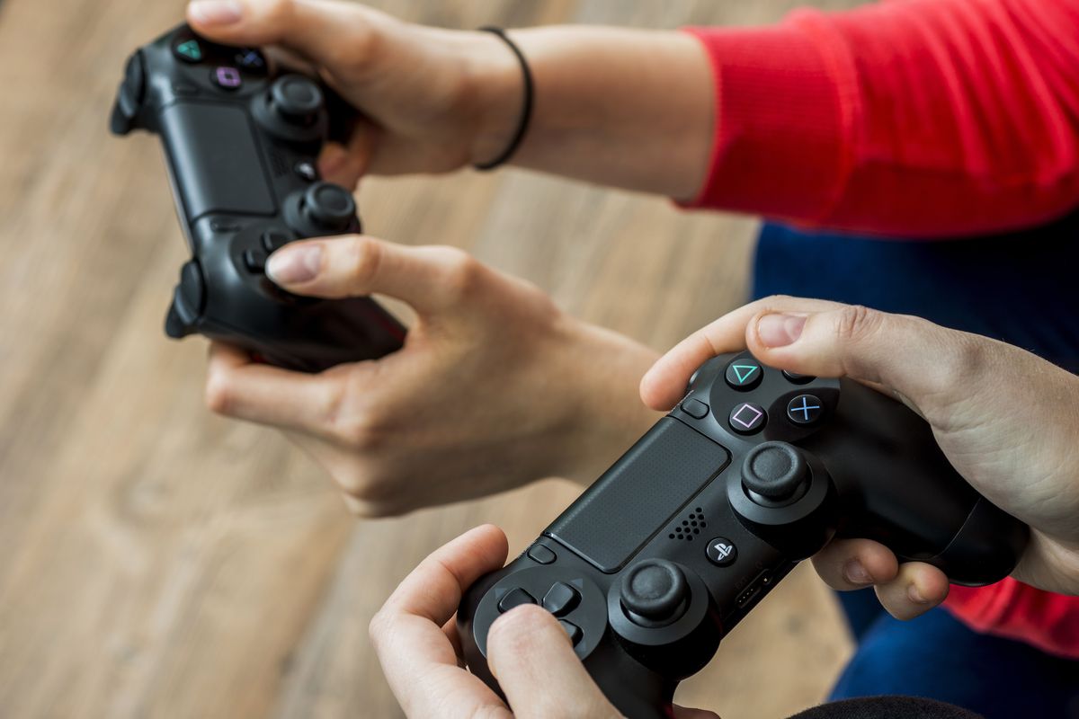 hands from two people are pictured holding PlayStation controllers 