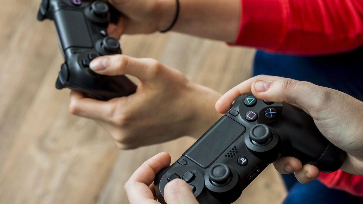 hands from two people are pictured holding PlayStation controllers