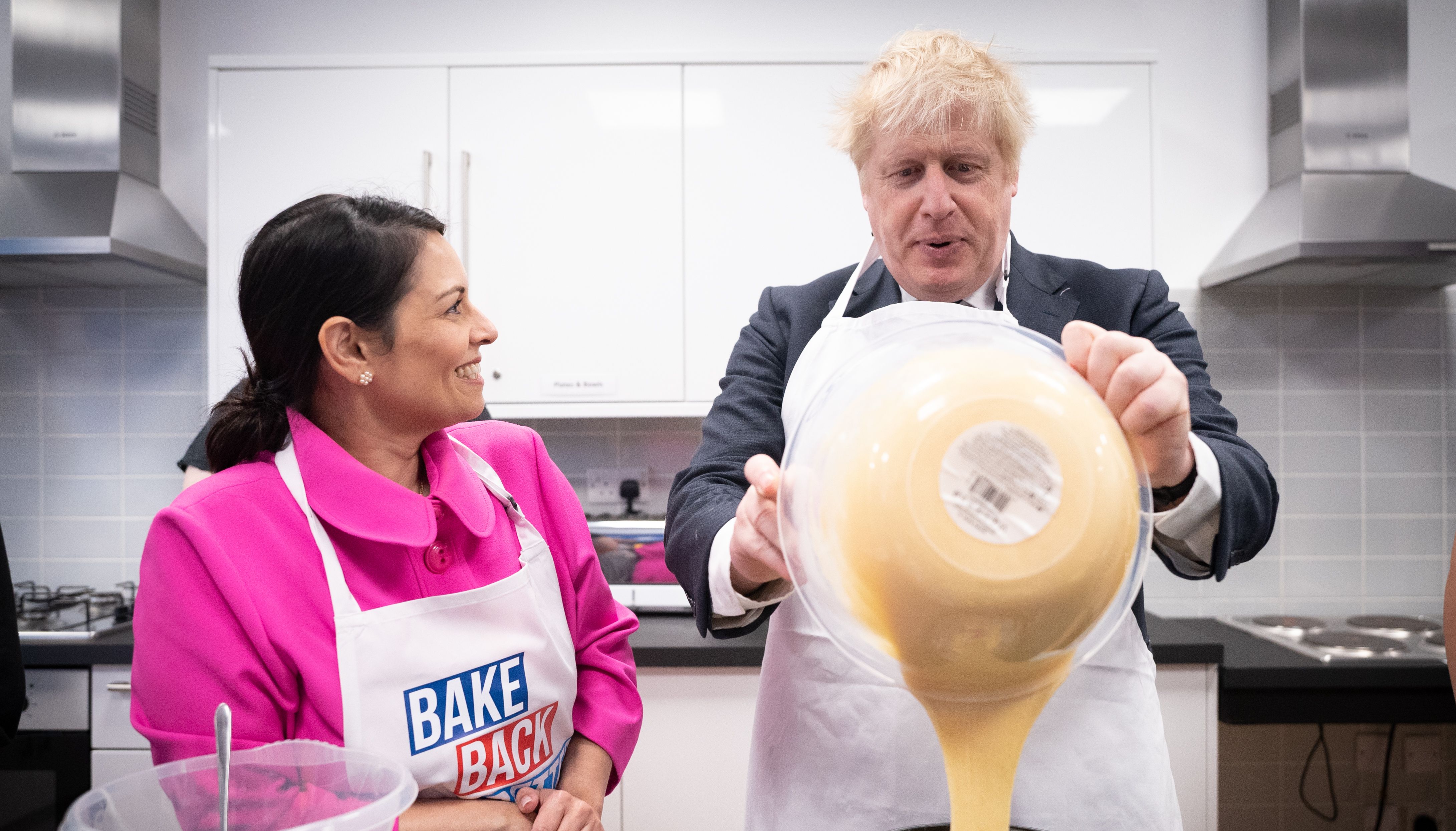 Home Secretary Priti Patel looks on as Prime Minister Boris Johnson tries his hand at baking during a visit to the HideOut Youth Zone, in Manchester.