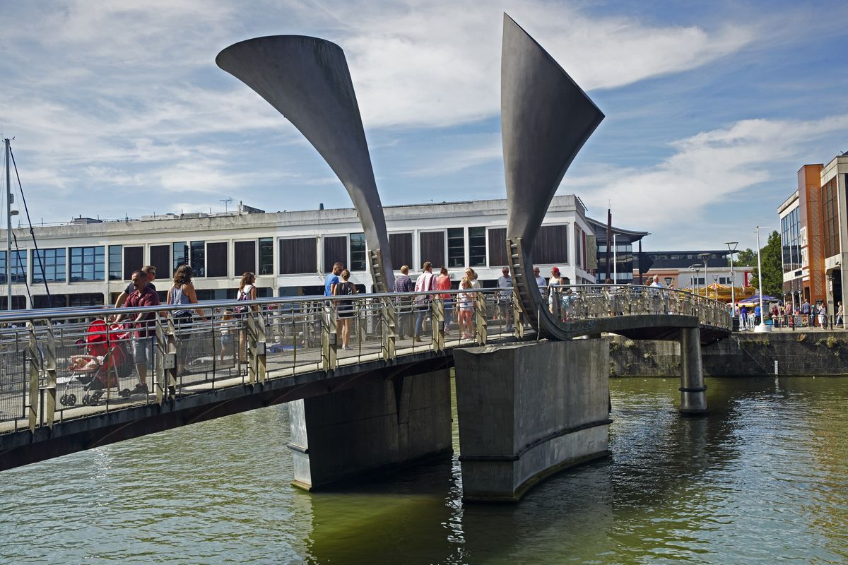 Horned sculptures and people crossing along Pero's footbridge on the redeveloped waterfront of Bristol's Millennium square