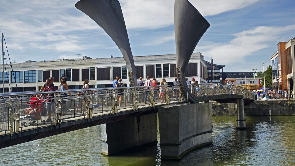 Horned sculptures and people crossing along Pero's footbridge on the redeveloped waterfront of Bristol's Millennium square