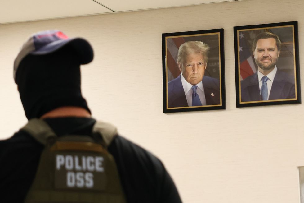Ice agent in front of portraits of Trump and JD Vance