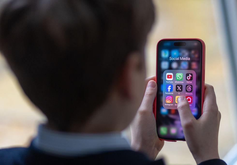 In this photo illustration a a 12-year-old school boy looks at a iPhone screen A 12-year-old boy looks at an iPhone screen showing various social media apps including TikTok, Facebook and X