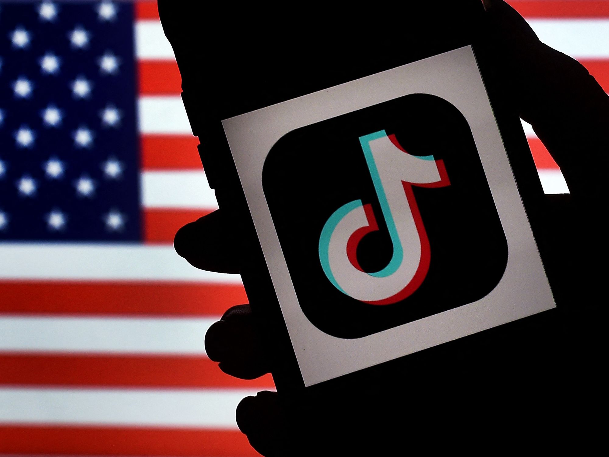 In this photo illustration, the social media application logo, TikTok is displayed on the screen of an iPhone on an American flag background