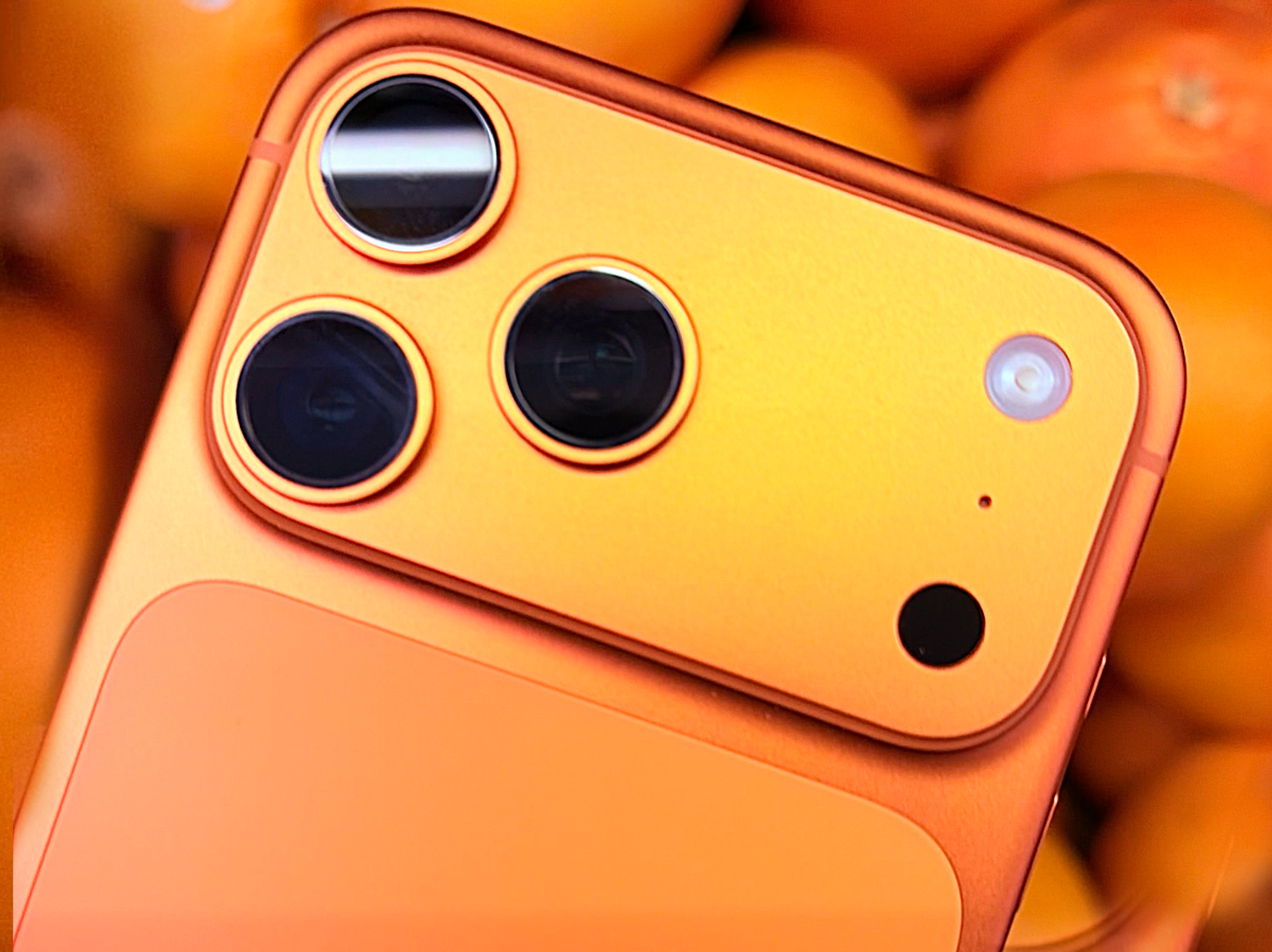 iPhone 17 Pro in Cosmic Orange with some oranges behind it