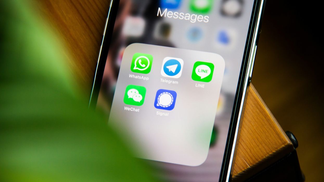 iphone pictured on table with folder of messaging services shown on-screen including whatsap, telegram and signal