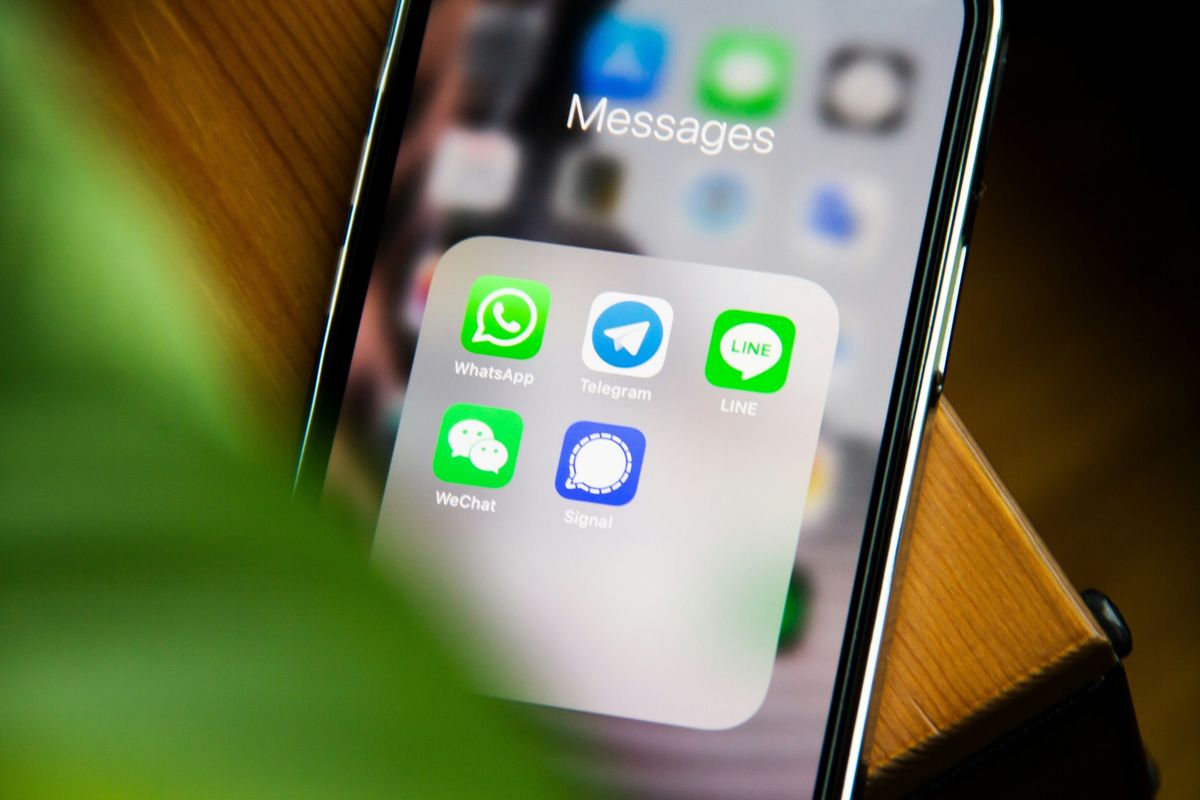 iphone placed on a table with a folder of messaging apps pictured on-screen 