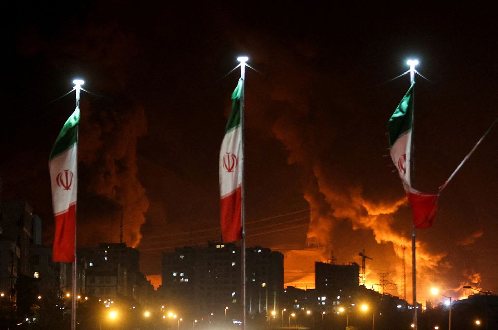 Iranian flags fly as fire and smoke from an Israeli attack on Sharan Oil depot rise