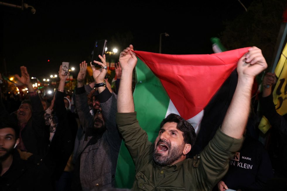 Iranians celebrating the attack on Israel holding a Palestinian flag