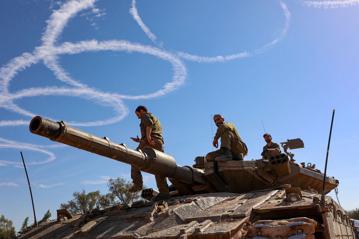 Israeli troops gather stand atop a tank on the border with the Gaza Strip on November 30, 2023