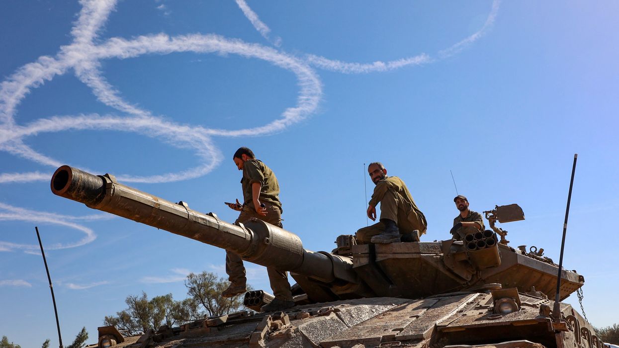 Israeli troops gather stand atop a tank on the border with the Gaza Strip on November 30, 2023