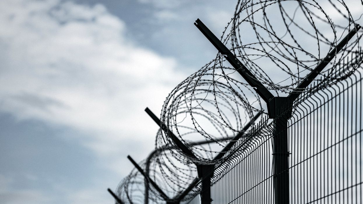 Jail or border fence with razor wire against dark sky.