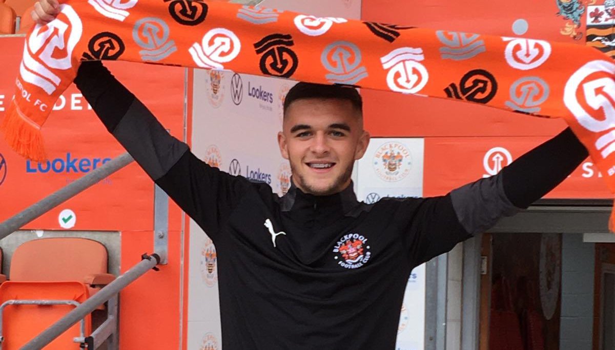 Jake Daniels holding a Blackpool scarf aloft.