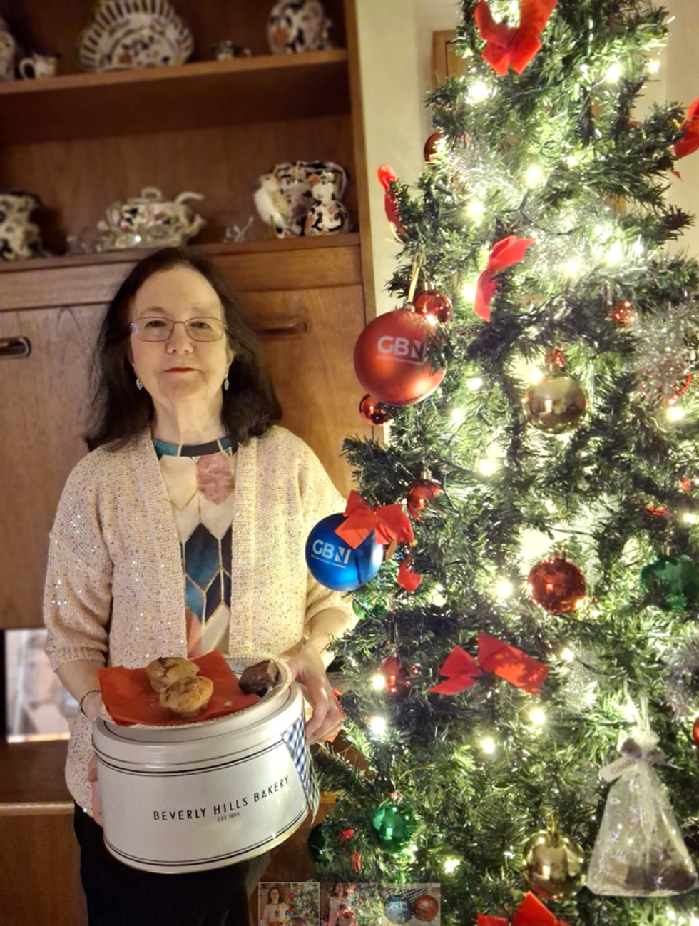 Jane stands beside her Christmas tree holding her tin of baked goods