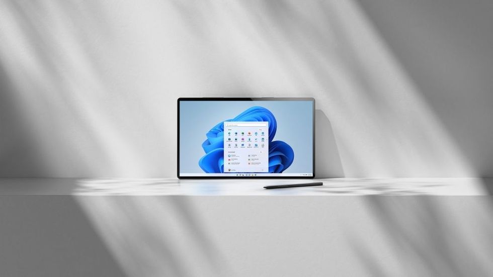 Laptop open displaying Windows 11 next to smart pen on white shelf