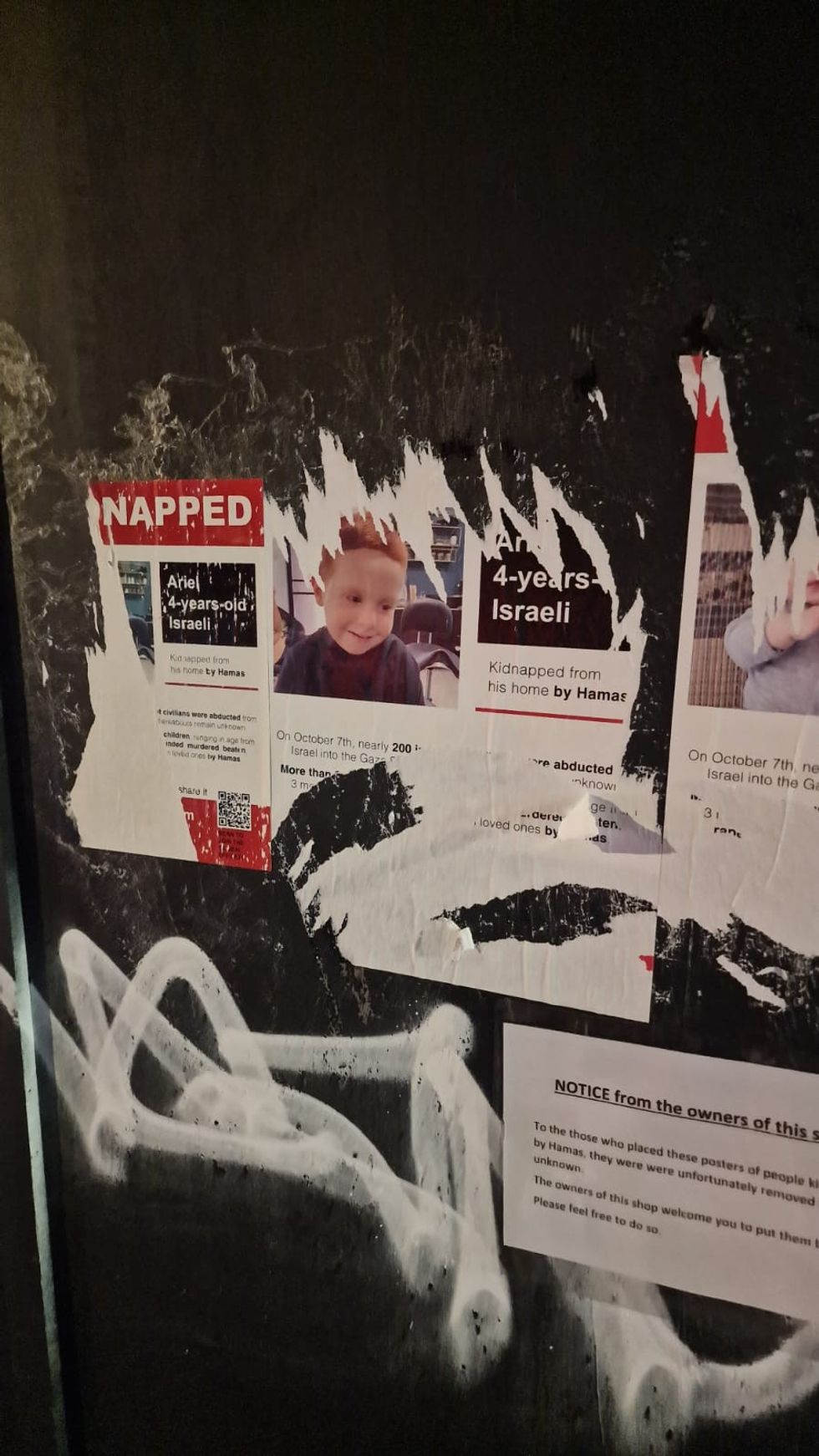 Large sections of the posters have been torn down from a boarded-up shop