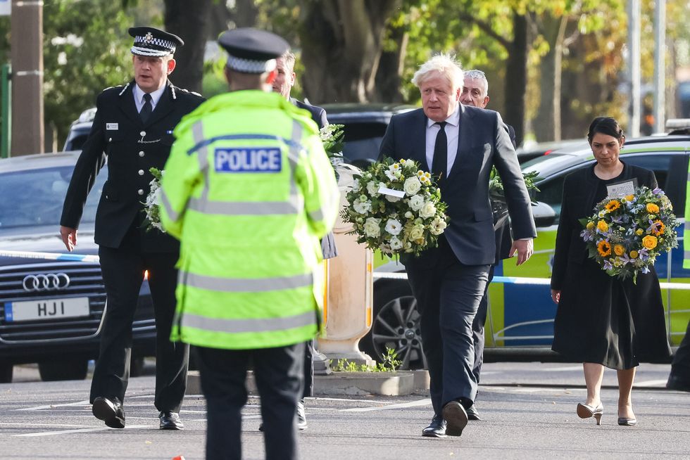 (left to right) Chief Constable Ben-Julian Harrington, Prime Minister Boris Johnson, and Home Secretary Priti Patel carry flowers as they arrive at the scene near Belfairs Methodist Church in Eastwood Road North, Leigh-on-Sea, Essex, where Conservative MP Sir David Amess died after he was stabbed several times at a constituency surgery on Friday. Picture date: Saturday October 16, 2021.