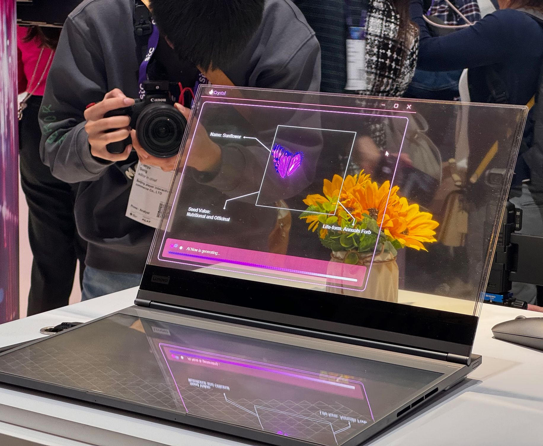 lenovo concept laptop with a transparent screen shown on the mwc tradeshow floor with objects seen through the glass