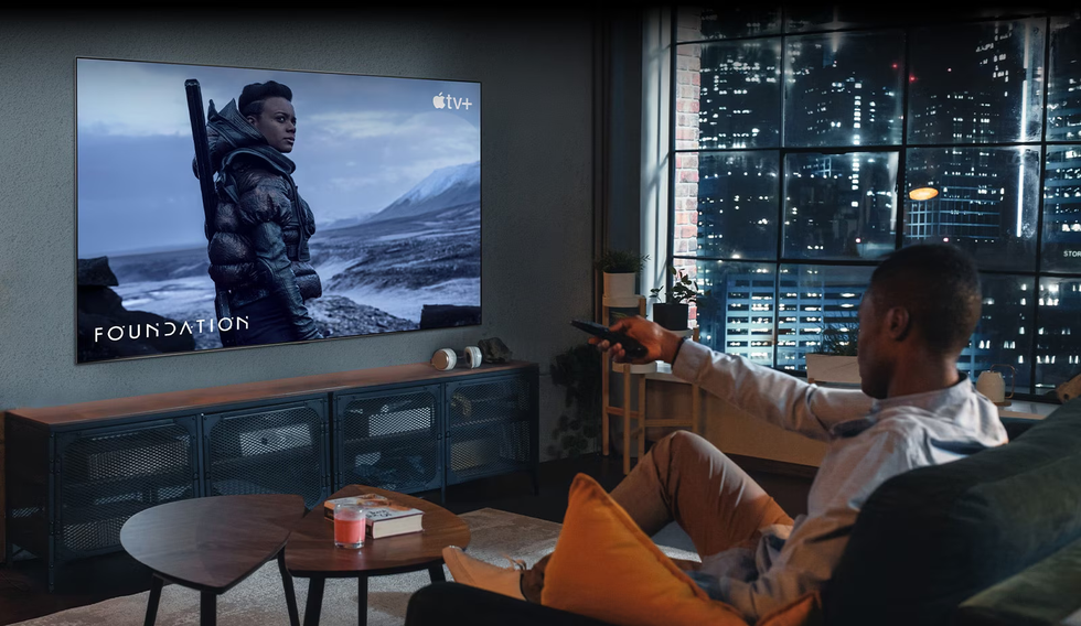 lg smart tv mounted on the wall with a man sitting on the sofa pointing the remote at the screen