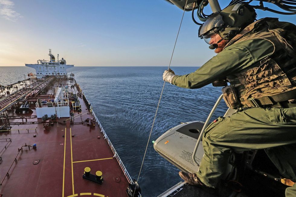 Man about to rappel down from helicopter above Russian shadow fleet vessel