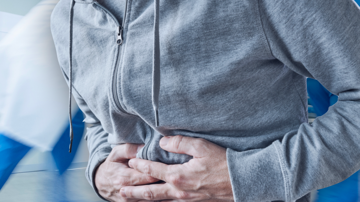 Man holding his stomach in pain in front of a busy hospital ward