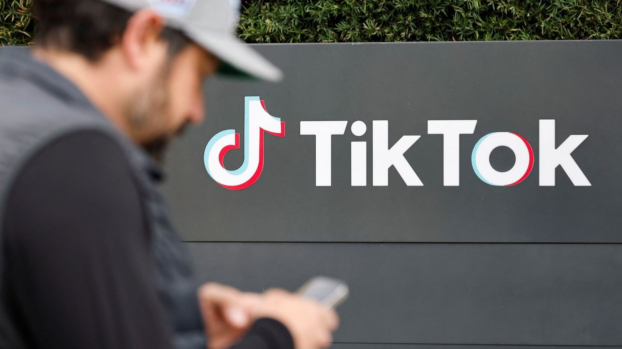 man in baseball hat pictured with smartphone outside of the TikTok sign on headquarters building