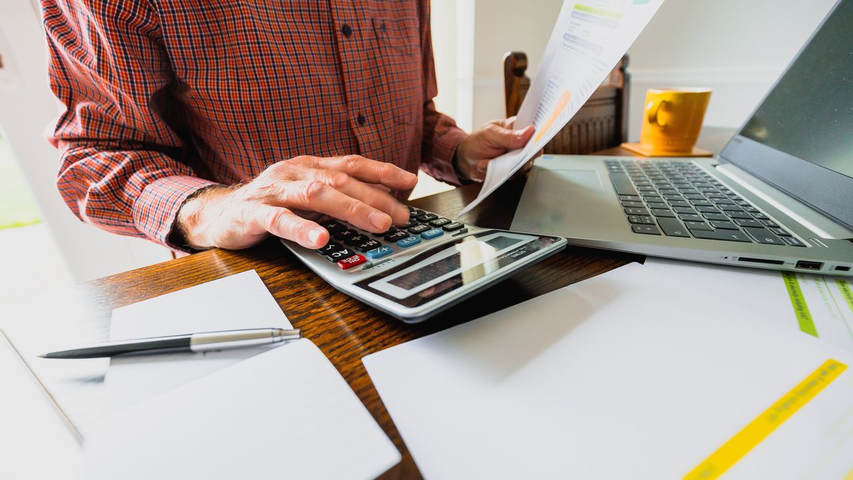 Man looks at calculator and documents with laptop in front of him