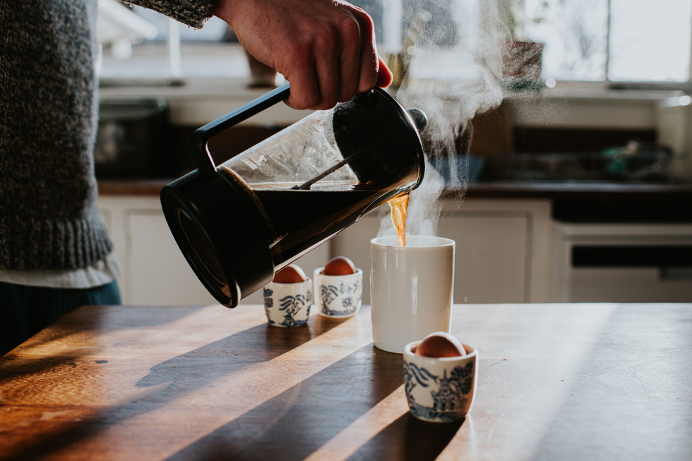 Man pouring a French press into a white mug on a wooden surface in a kitchen