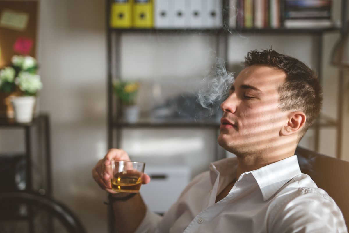 Man sitting back in a chair smoking and drinking 