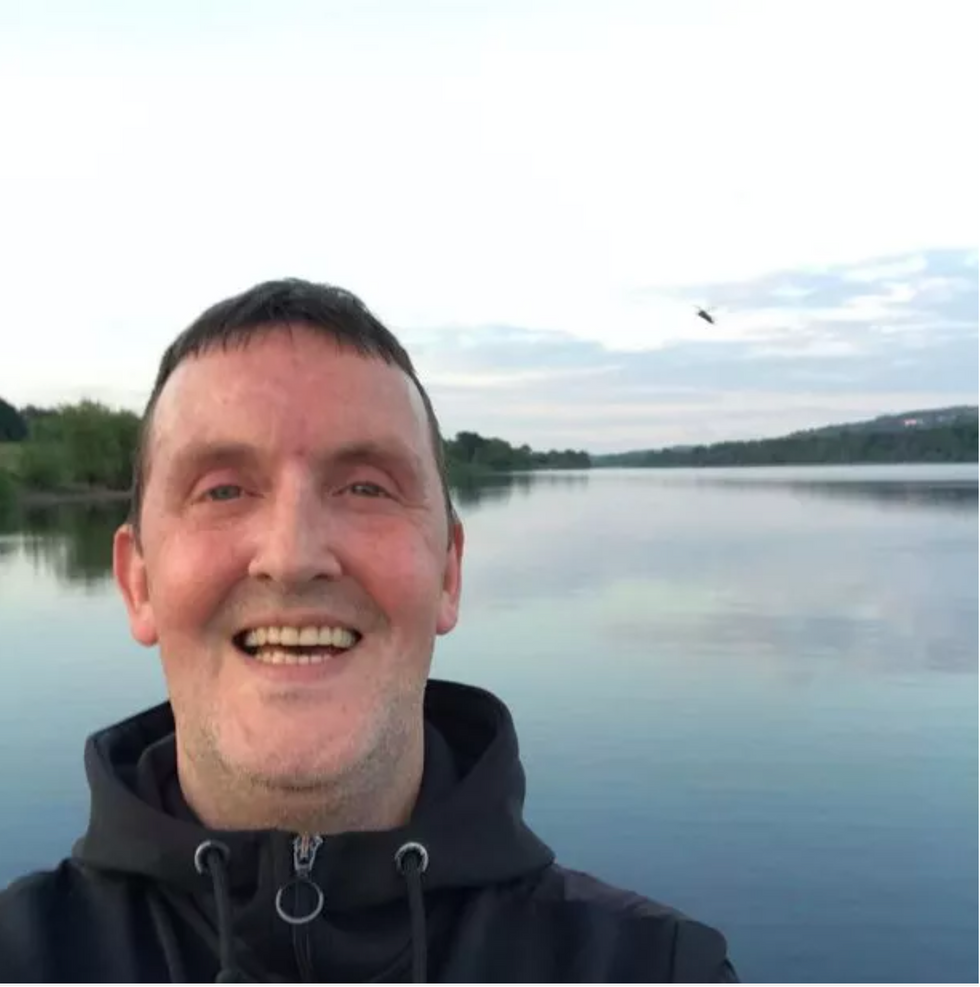 Man smiles in selfie by a lake