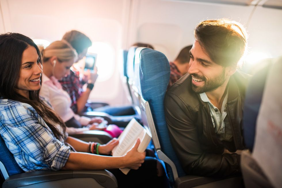 Man speaking to the woman siting behind him on a flight